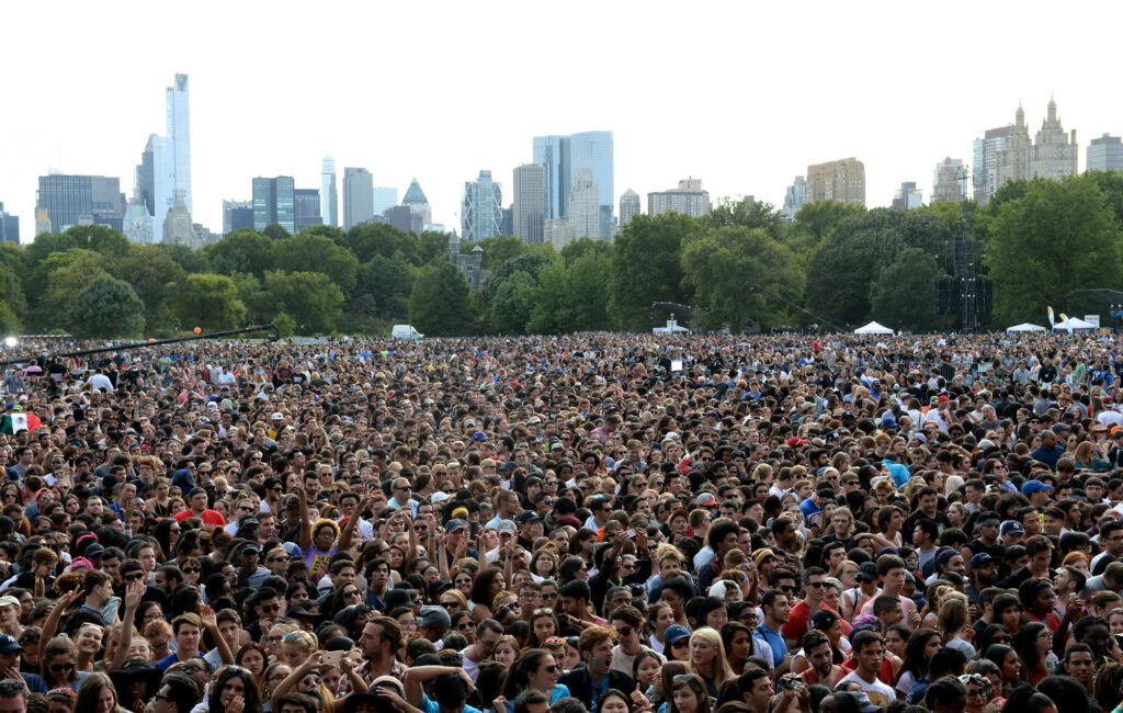 A wide-angle photo of a large, diverse crowd gathered on the Great Lawn of Central Park, with a stage in the background during the Global Citizen Festival